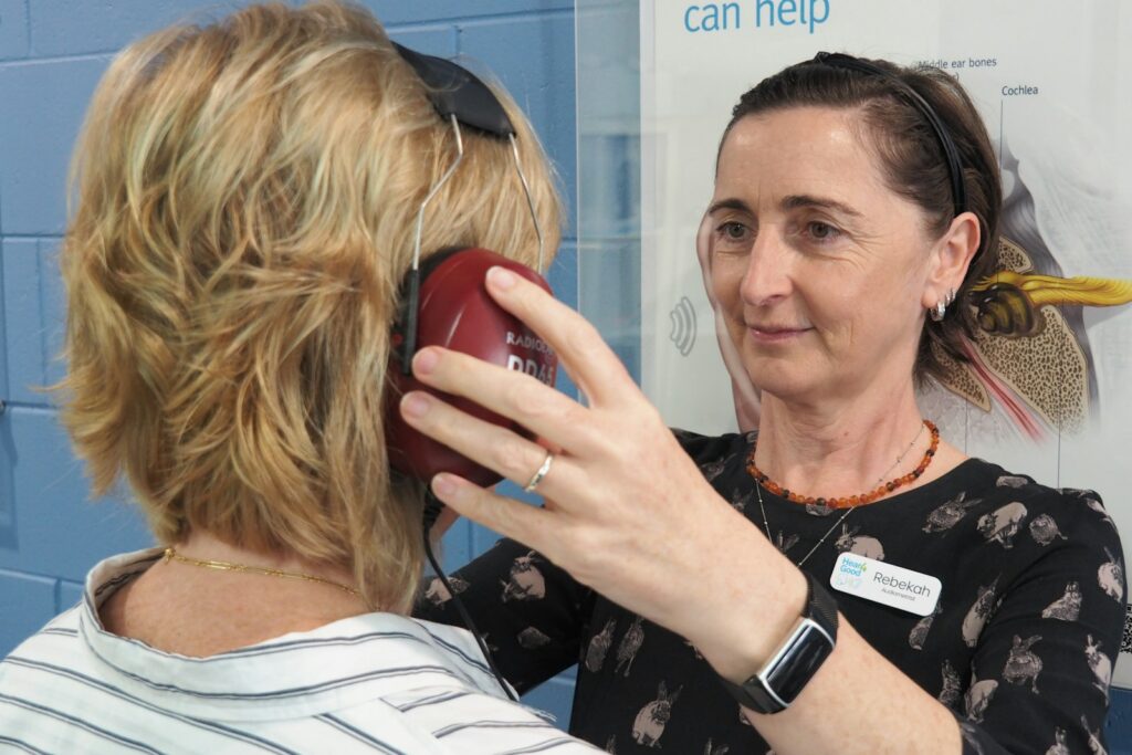 Audiologist placing headphones on a woman ahead of a hearing test